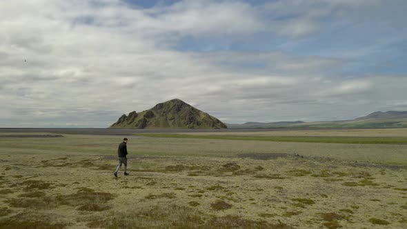 Aerial drone view passing a man walking over a green field, towards a mountain, in Iceland