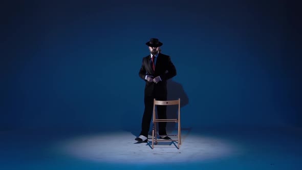 Elegant Man in a Black Hat Is Dancing an Erotic Dance. Spotlight on a Blue Background. Close Up