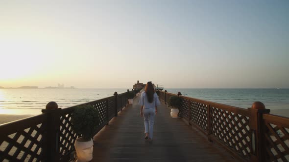 Woman Walking on the Wooden Pier During Sunset with Dubai Skyline in the Background