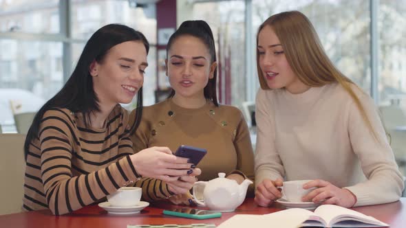 Close-up of Three Caucasian Female Friends Looking at Smartphone Screen in Restaurant and Talking