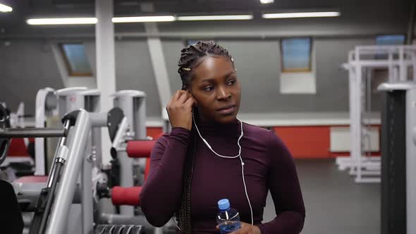 Sports Training Black Woman Walks in the Empty Gym and Drinking Water From the Bottle Putting in Her