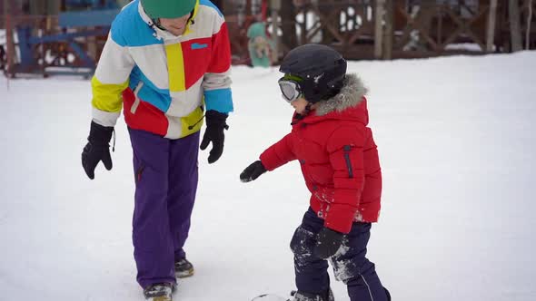 Young Man Snowboard Instructor Tiches Little Boy How To Ride a Snowboard. Winter Activities Concept