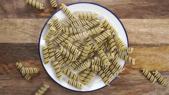 Uncooked pea fusilli pasta. Falling green vegetable macaroni on a plate on a wooden table