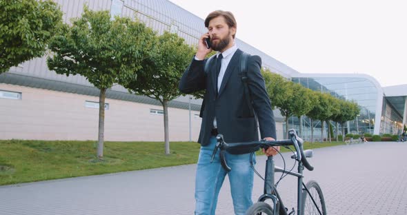 Modern Man in Stylish Clothes Which Going Down with His Bike on the Street and Talking on Smartphone