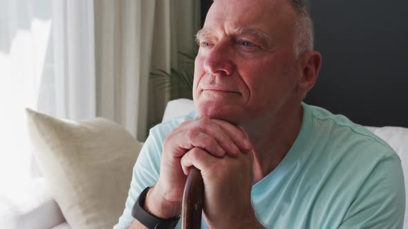 Close up of caucasian senior man holding walking stick while sitting on the couch at home