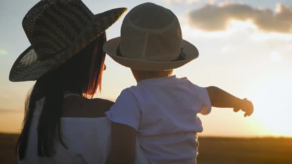 Mother and Little Son Playing on Meadow, Boy Raising Up Hands at Wonderful Sunset 