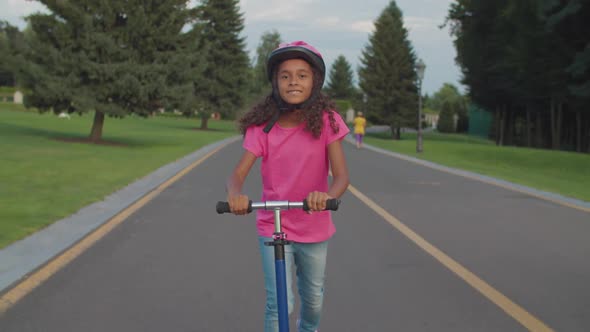 Active African Little Girl Riding Scooter in Park