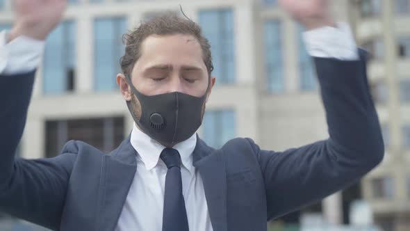 Stressed Man in Covid-19 Face Mask Standing Outdoors in Front of Office Building and Holding Head in