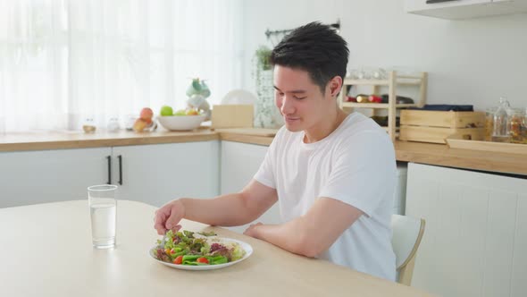 Asian attractive handsome male eating green salad in kitchen at home.