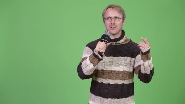 Studio Shot of Blonde Handsome Man Using Microphone and Looking Guilty