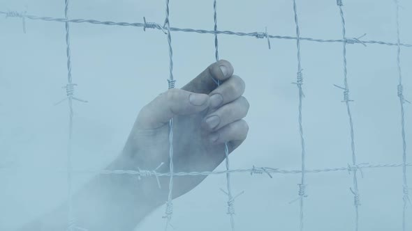 Hand Grasps Wire Fence With Smoke Passing