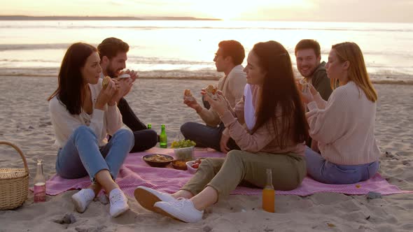 Happy Friends Eating Sandwiches at Picnic on Beach