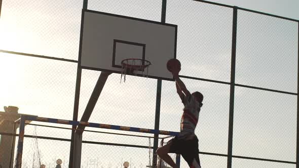 Caucasian Male Player in Streetball Doing Twohanded Slam Dunk on Outdoor Sports Ground in Slowmotion
