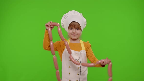Child Girl Dressed As Cook Chef in Apron Puts on a Bunch of Sausages Around Her Neck Fooling Around
