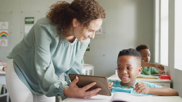 Video of happy caucasian female teacher explaining lesson on tablet to african american boy alt