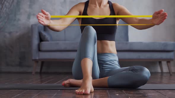 Young and sporty girl in sportswear is doing exercises in home interior using resistance band.