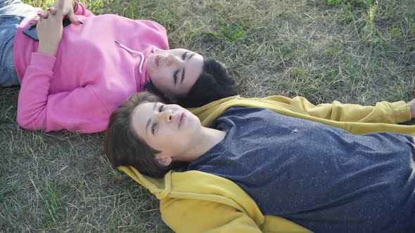 Top View Smiling Loving Teenage Boyfriend and Girlfriend Lying on Green Grass on Meadow Talking