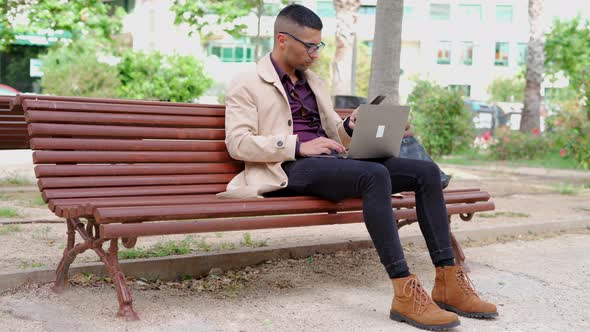Young businessman in trendy outfit speaking on phone on bench