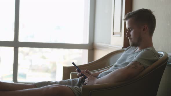 Young Bearded Man Uses Smartphone While Sitting on a Sofa at Home