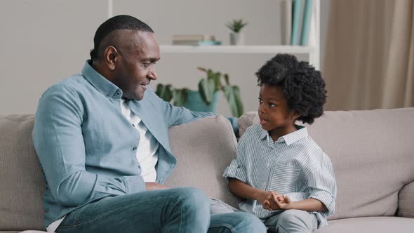 Mature African American Man Chatting with Kid Girl Sitting on Sofa in Room Loving Caring Father Asks