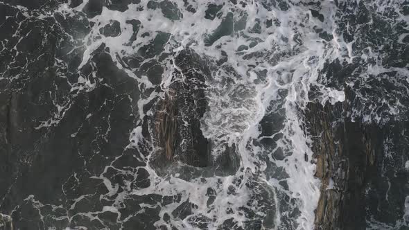 Sea foam and waves curling around two exposed rocks at sunrise AERIAL TOP DOWN