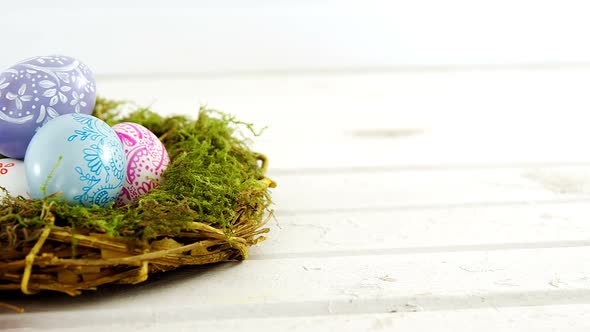 Painted Easter eggs in the nest on wooden surface