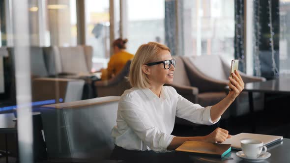 Elegant Mature Blond Lady Talking on Smartphone Making Video Call in Cafe