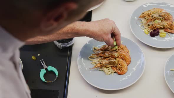 Caucasian male chef wearing chefs whites in a restaurant kitchen, putting food on a plate