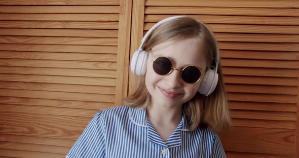 Cute Girl with Round Sunglasses and Wireless Headphones Listening to Music