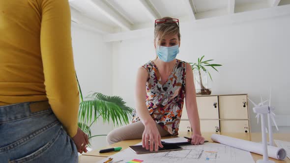 Two woman wearing face mask discussing over documents on table at office