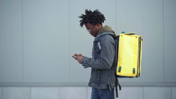 Side View of Handsome African American Male Courier Walking in Urban City with Yellow Insulated Bag