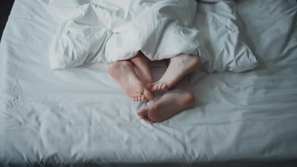 Bare Feet of a Loving Couple Lyuing Under Blanket and Petting in Bed