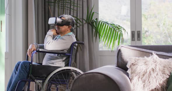 Happy mixed race senior man on wheelchair wearing vr headset and having fun at home