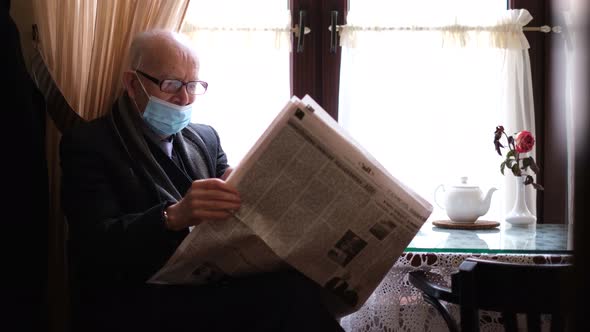 A Retired Man in a Mask Sits in a Cafe and Reads a Newspaper