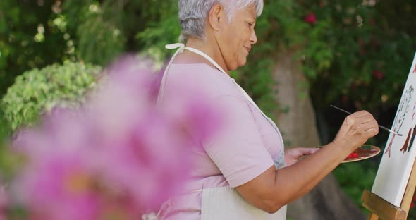 Video of happy biracial senior woman painting in garden