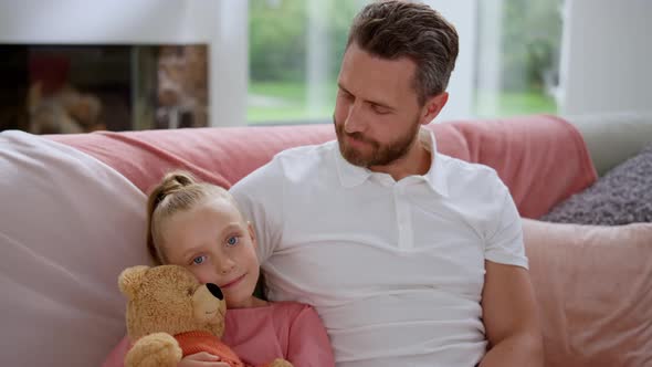 Cute Daughter Sitting on Couch with Father. Cheerful Man Looking at Small Girl