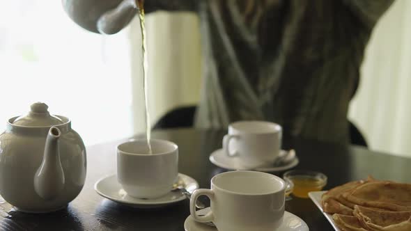Man Is Pouring Tea From Brewing Teapot To White Cup and Back, Close-up