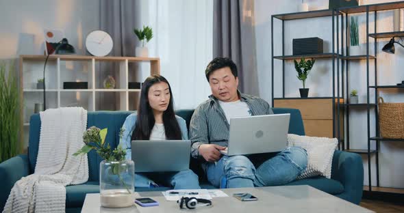 Asian Father and Daughter Sitting Together on Comfortable Sofa at Home and Use their Computers