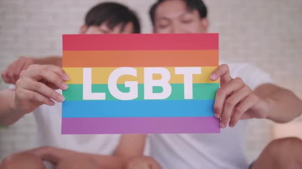 Happy gay Asian couple showing their love with rainbow flag.