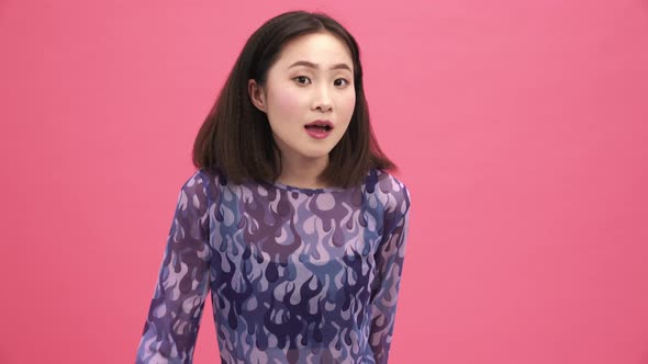 Cheerful Asian woman looking around and showing silence gesture at the camera