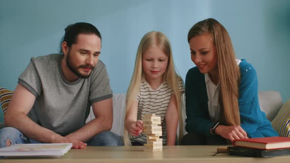 Blonde Girl Plays Jenga with Mom and Dad and Loses