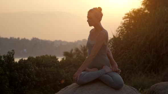 Practitioner Sits in Revolved Lotus Pose on Rock Slow Motion