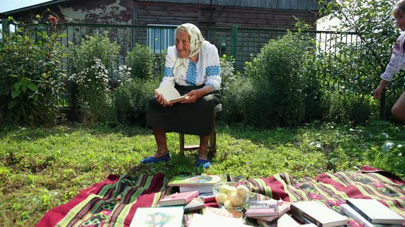 An Old Grandmother is Sitting on the Street and Reading a Book