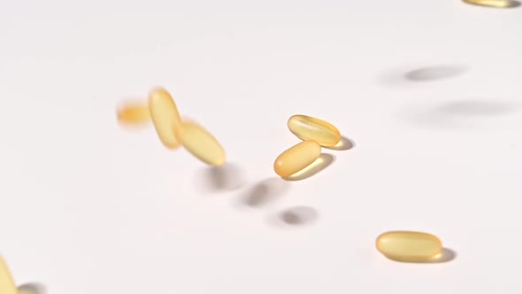 Closeup of Falling Transparent Yellow Capsules Over White Backdrop