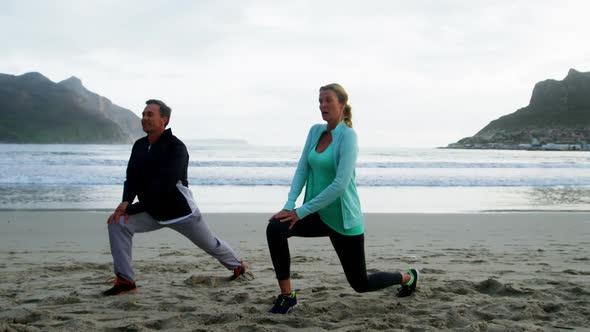 Mature couple performing stretching exercise on beach