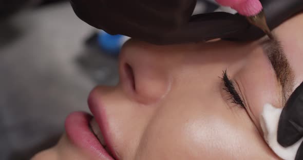 The master makes permanent eyebrow makeup with the help of a tattoo machine