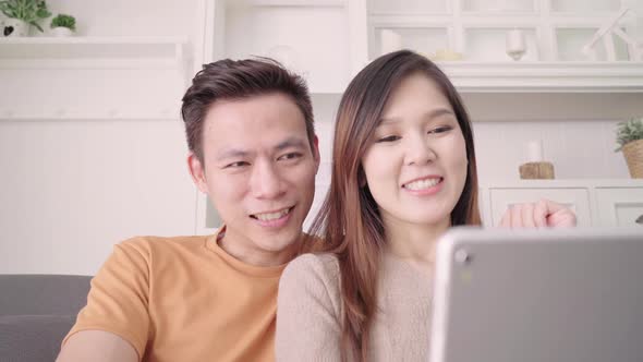 Asian couple using tablet VIDEO Call with friend in living room while lying when relaxed.