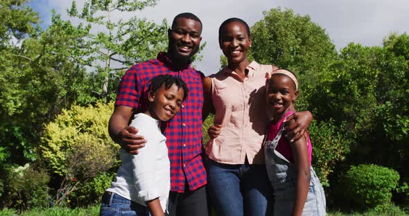 Portrait of smiling african american parents embracing with son and daughter in garden