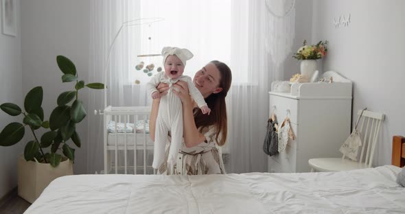 Young Beautiful Mother Lifts Her Adorable Newborn Baby Up and Down