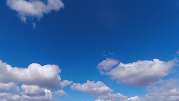 Puffy cumulus clouds form and travel through blue sky, time lapse